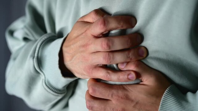A man is having a heart attack.
The man is clutching his chest with his hands, trying to ease the pain and palpitations.