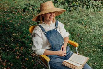 Person relaxing and reading book in garden under apple tree in autumn