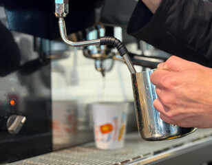 Barista preparing milk in a coffee machine for adding to coffee. Female hands are making coffee using professional metal machine in cafe. Barista is heating milk, whipping foam with frother, steam. 