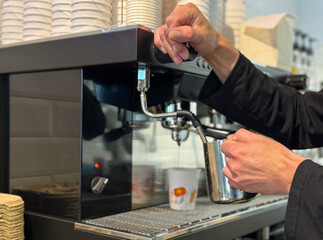 Barista preparing milk in a coffee machine for adding to coffee. Female hands are making coffee using professional metal machine in cafe. Barista is heating milk, whipping foam with frother, steam. 