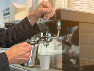 Barista preparing milk in a coffee machine for adding to coffee. Female hands are making coffee using professional metal machine in cafe. Barista is heating milk, whipping foam with frother, steam. 