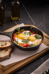Shakshuka with poached eggs and vegetables served in skillet with bread
