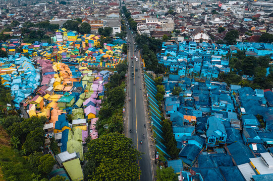 Aerial view of vibrant colors explode across the Jodipan Rainbow Village, a stark contrast to the monochrome buildings on the other side of the road, Malang, Malang, Indonesia.