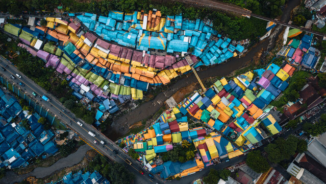 Aerial view of a vibrant tapestry of rainbow-colored homes nestled along the riverbanks of Jodipan Rainbow Village, a striking contrast to the lush greenery, Malang, Indonesia.