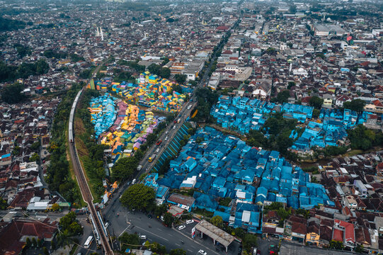 Aerial view of vibrant rainbow hues splashed across the Jodipan Rainbow Village contrasting with the cool blues of the adjacent neighborhood, Malang, Malang, Indonesia.