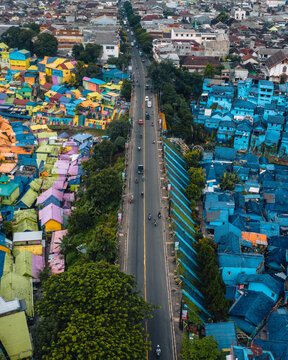 Aerial view of a vibrant contrast between rainbow hues and deep blues defining homes divided by a central road, Jodipan Rainbow Village, Malang, Indonesia.