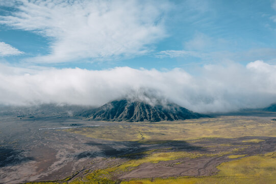 Aerial view of the dark peak of Mt. Bromo piercing through a sea of fluffy white clouds, contrasting with the arid landscape below, Mt. Bromo, East Java, Indonesia.