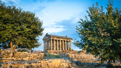 The Temple of Garni in Armenia captured at golden hour, framed by trees and ancient ruins. A classical Greco-Roman structure set in a dramatic mountain landscape