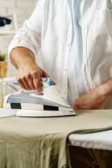 Fototapeta premium Man ironing a shirt at home during daylight hours for everyday chores