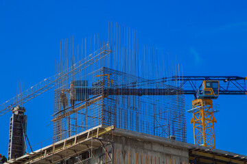 Close-up of the upper floor of the building under construction, you can see the reinforcement, mesh and formwork, next to the crane against the blue sky. Concept of construction, erection of buildings