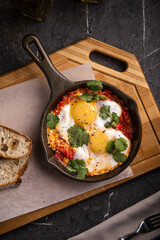 Shakshuka with poached eggs and vegetables served in skillet with bread