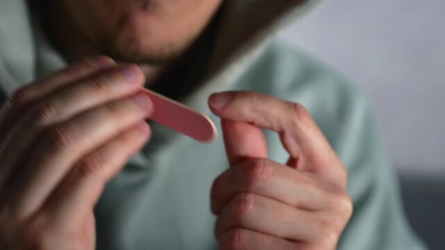 Trimming and filing nails with a nail file.
A man trims his long fingernails and files the sharp edges with a nail file.