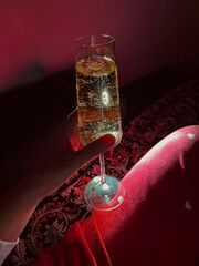 Close-up of a female hand holding a champagne glass in a warm red and gold festive atmosphere. Holiday scene, perfect for seasonal and lifestyle concepts.