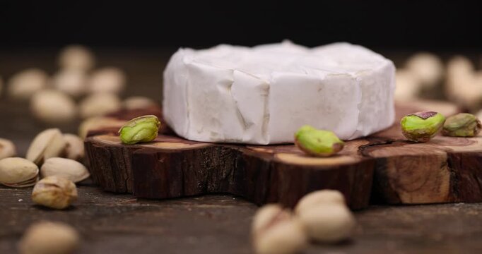 unshelled pistachios are on the table along with whole cheese in white mold, delicious white soft cheese in mold and a large number of salted pistachios with cracked shells.