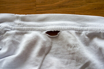Close-up of hole in worn out wrinkled white short sleeve shirt laying on oak wooden table at living room. Photo taken October 6th, 2025, Zurich, Switzerland.