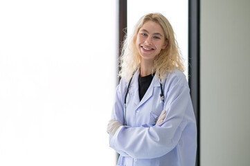 Portrait of female doctor wearing medical gloves stands by a large window. with stethoscope on the neck. Smiling and look at the camera.
