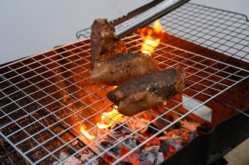 Grilled beef steak on barbecue grill over charcoal fire with tongs. Tender meat sizzling on a barbecue grill with flames below.