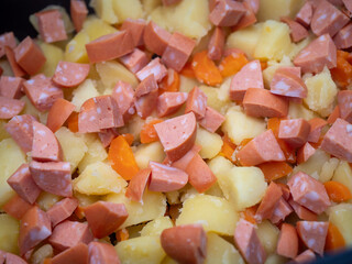 Detailný záber na zemiaky, mrkvu a nakrájané špekáčky zmiešané dohromady, pripravené na zapekanie tradičných francúzskych zemiakov.