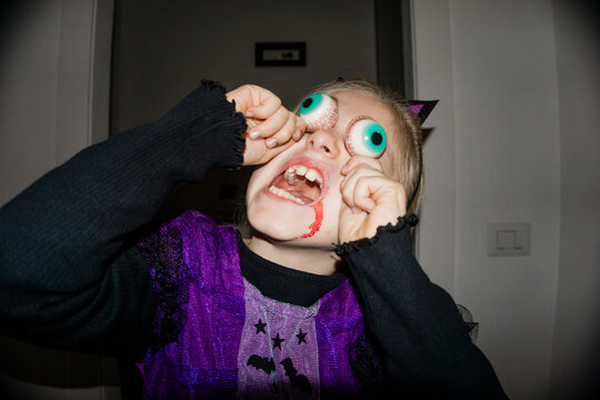 A young girl in a witch costume with fake blood and eyeballs on her fingers makes a funny face for Halloween.