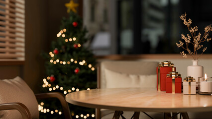 Present gift box and candle on wooden round table aside armchair and Christmas tree in a living room