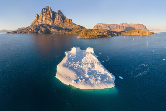 The mountain and island of Uummannaq with the village of the same name in western Greenland in one of the fjords. Floating icebergs, global warming, and climate change. Summer time, aerial view.