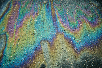 Oil spill forming colorful iridescent patterns on dark asphalt pavement