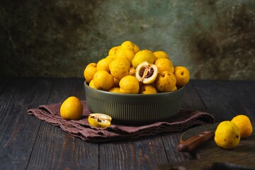 Japanese quince fruits, or Chaenomeles, in a ceramic bowl against a dark wooden background.