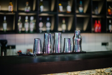 A set of metal cocktail glasses and shakers on a dark bar counter