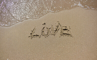 Love word is written on sand and soft sea wave next to it top view