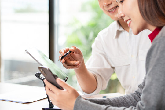 Two asian business persons working together. Businessman brainstorming, having a discussion with her colleague about work project, working on laptop computer at modern office. Business teamwork. - Powered by Adobe