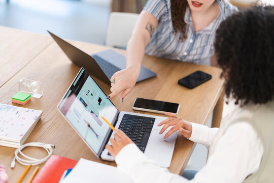 Two women collaborate on a laptop, discussing online content. One woman points to the screen while the other uses the trackpad.