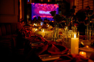Close-up of a long table with flowers and burning candles in a dark room