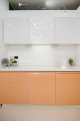Detail of a contemporary kitchen with orange lower and white upper cabinets.