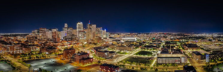 Aerial view of glowing skyscrapers pierce the dark sky, casting a warm light over the cityscape, illuminating the streets below, Denver, Colorado, United States.