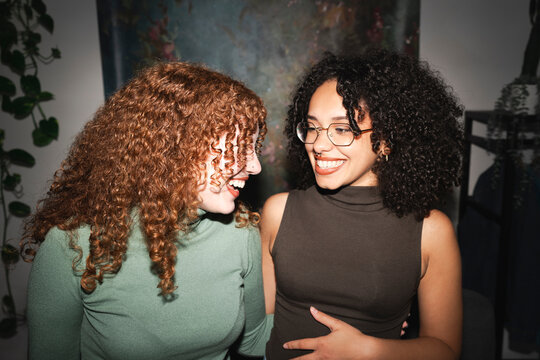 Two young women with curly hair share a laugh, their faces illuminated by warm light, conveying joy and connection.