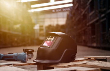 Welding helmet and angle grinder in sunlit warehouse