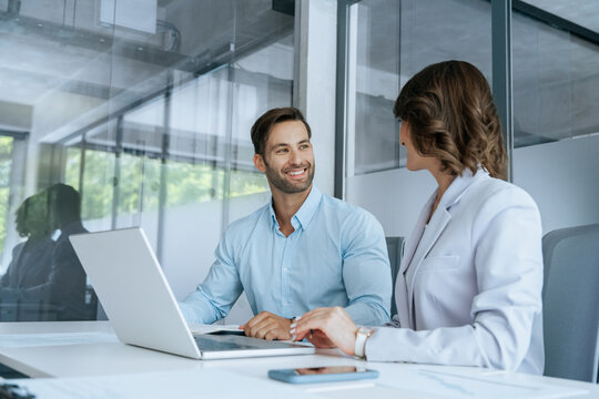 Two busy diverse colleagues, group team of professional business people discussing project sitting at desk. Mature Latin hispanic woman and European young man working using laptop computer in office