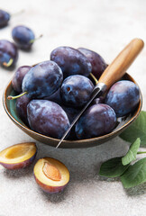 Fresh plums in bowl with knife on gray background