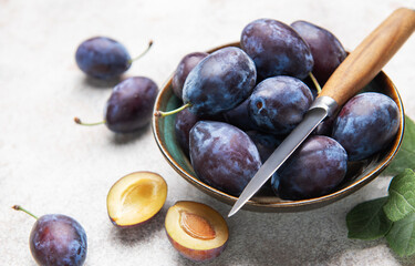 Fresh plums in bowl with knife on gray background