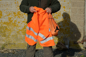 Cadrage serré sur un homme qui tient une chasuble orange dans les mains avant d'aller à la chasse