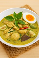 Thai green curry with fish balls, herbs, egg, and coconut-based broth—vibrant, aromatic, and served in a patterned bowl on woven mat