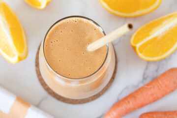 Orange and carrot smoothie in a glass on white marble table. Top view. Healthy blended breakfast drink.