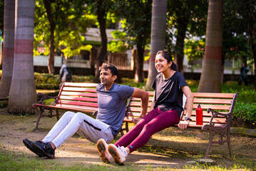Fototapeta premium Indian beautiful young couple tricep dips together outdoors in sunny park for fitness goals