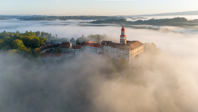 N&aacute;chod Castle at sunrise with fog in the valley engulfing the entire town of N&aacute;chod. Aerial view. Sunny summer or autumn day, Czech Republic