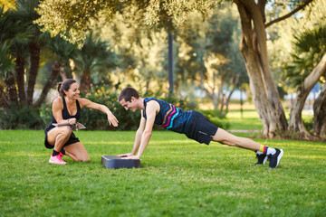 Personal trainer guiding man doing assisted push-ups outdoors