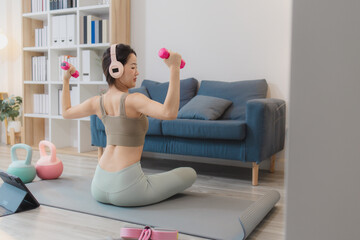 Fototapeta premium A young woman is exercising at home, practicing yoga and strength training with dumbbells and kettlebells on a mat. She follows her workout routine with focus and determination.