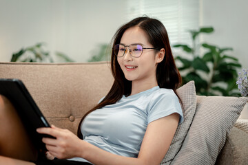 Woman wears blue light glasses reading tablet screen protecting eyes longevity lifestyle at home cozy living room digital content healthy habit
