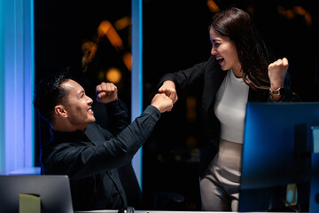 Young adult tech professionals celebrating project success with a fist bump late night in modern office AI agent coding triumph achievement