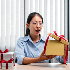 Happy woman is feeling excited during opening present box with red ribbon while looking into gift box