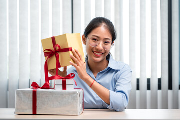 Happy woman is smiling and holding present box with red ribbon in the hands while preparing gift for celebrate